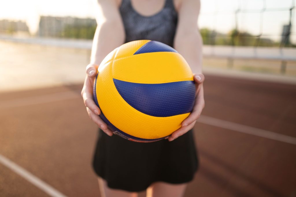 pessoa em uma quadra mostrando bola de vôlei com as mãos.