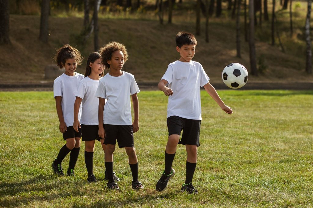 crianças enfileiradas para treinar com a bola no campo de futebol.