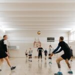 Jogadores adultos participam de uma aula de vôlei em uma quadra.