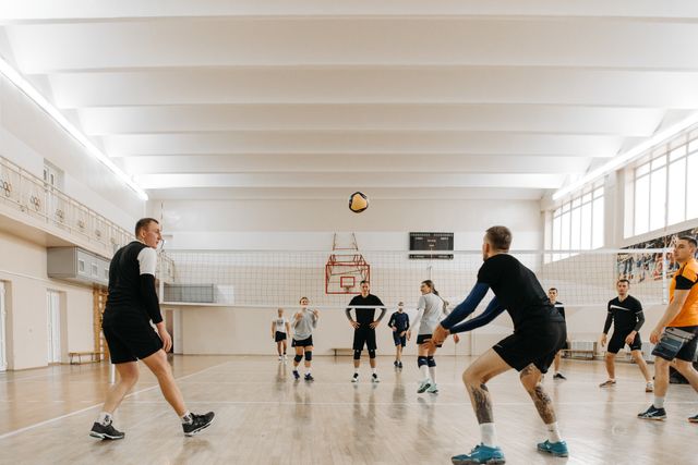 Jogadores adultos participam de uma aula de vôlei em uma quadra.