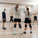Grupo de adultos jogando vôlei em quadra coberta.